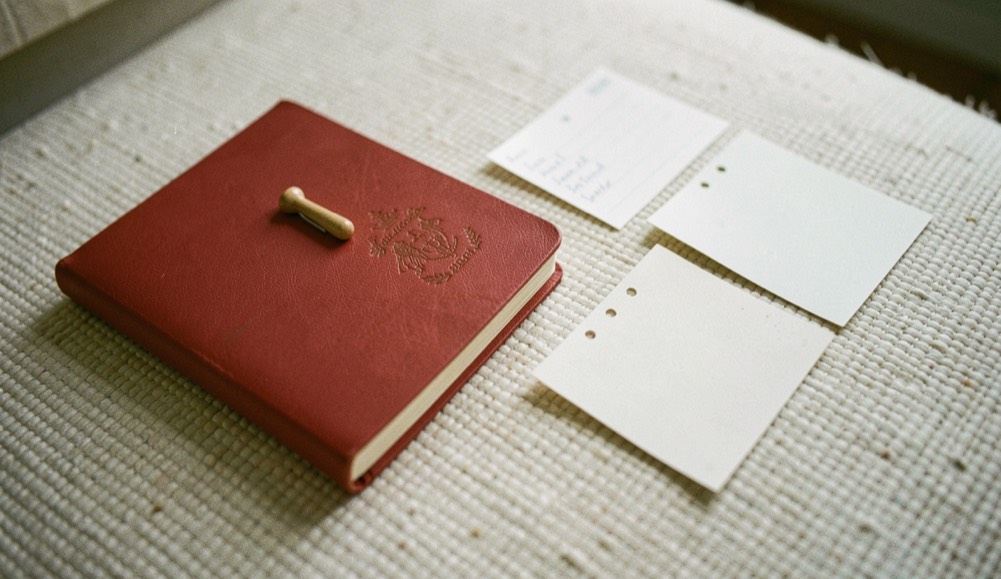 Petit carnet rouge fermé, trombone et fiches perforées alignés sur un tapis ivoire, cadrage rapproché